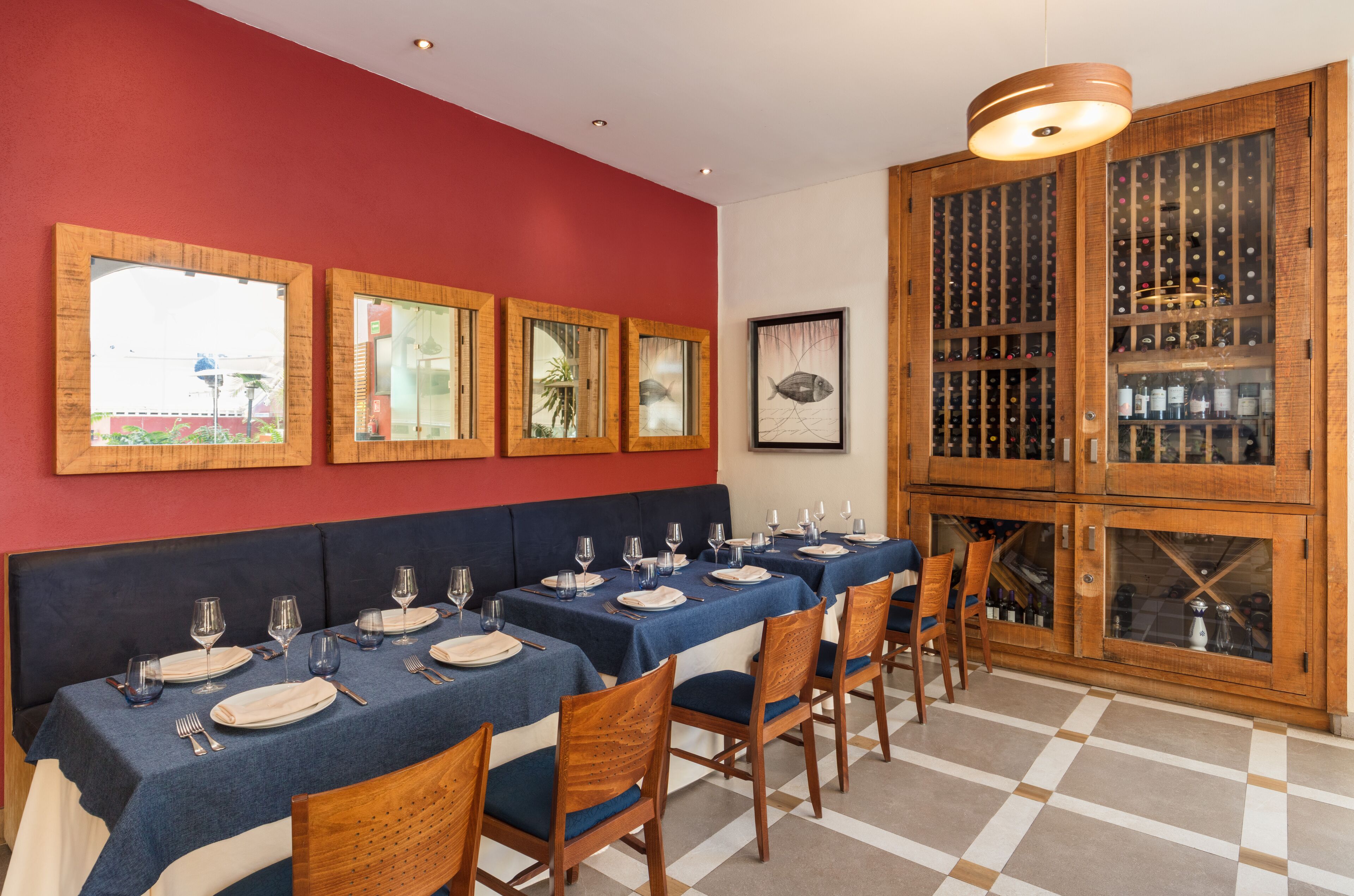 Un coin repas avec une longue table dressée pour le repas, des meubles en bois contenant des bouteilles de vin et des œuvres d’art encadrées accrochées au mur.
