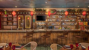Un bar avec des tabourets en bois, un téléviseur et des étagères remplies de bouteilles.