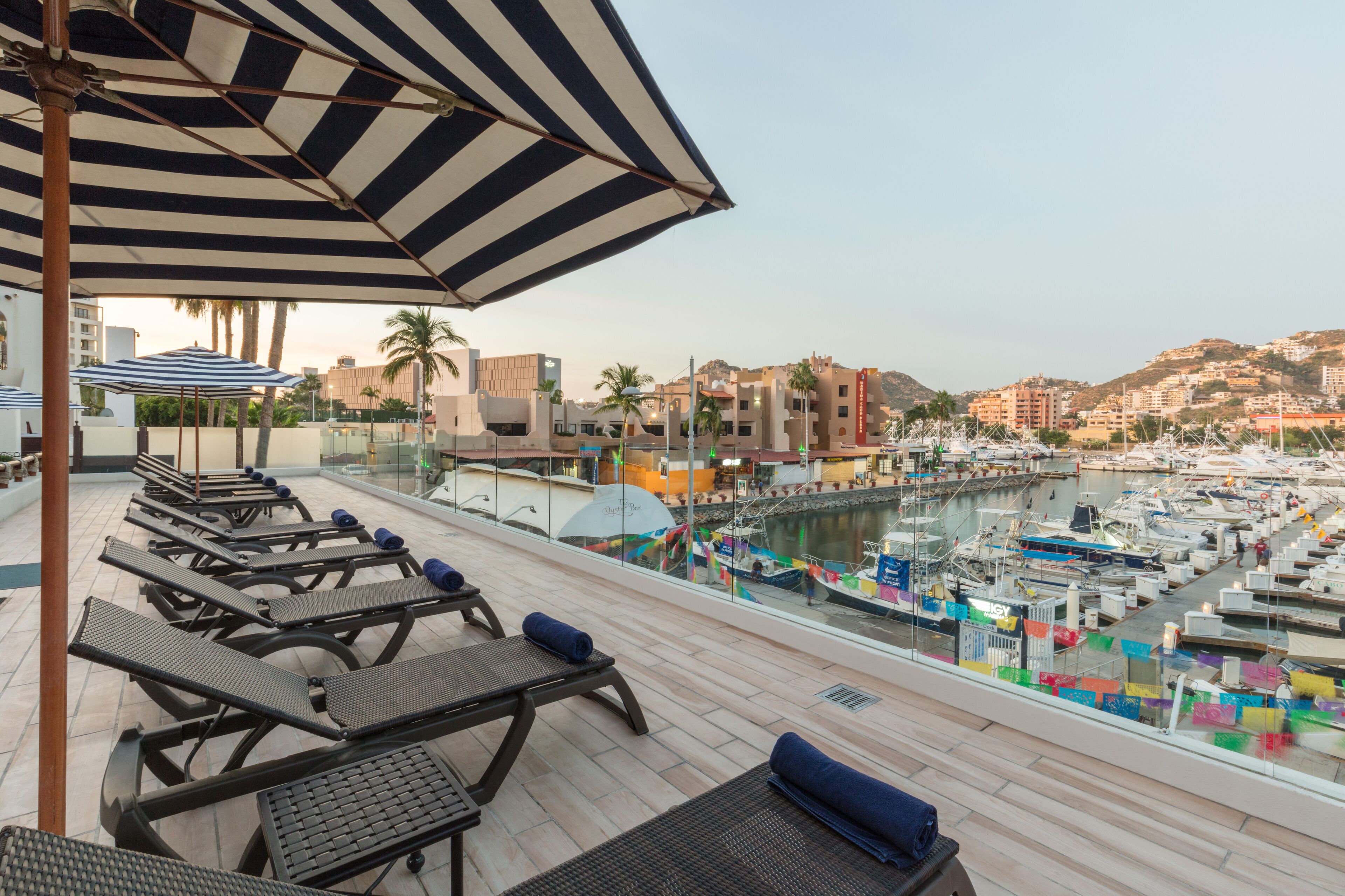 A rooftop terrace with sun loungers and a view of a marina with boats.