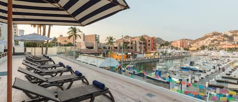 A rooftop terrace with sun loungers and a view of a marina with boats.
