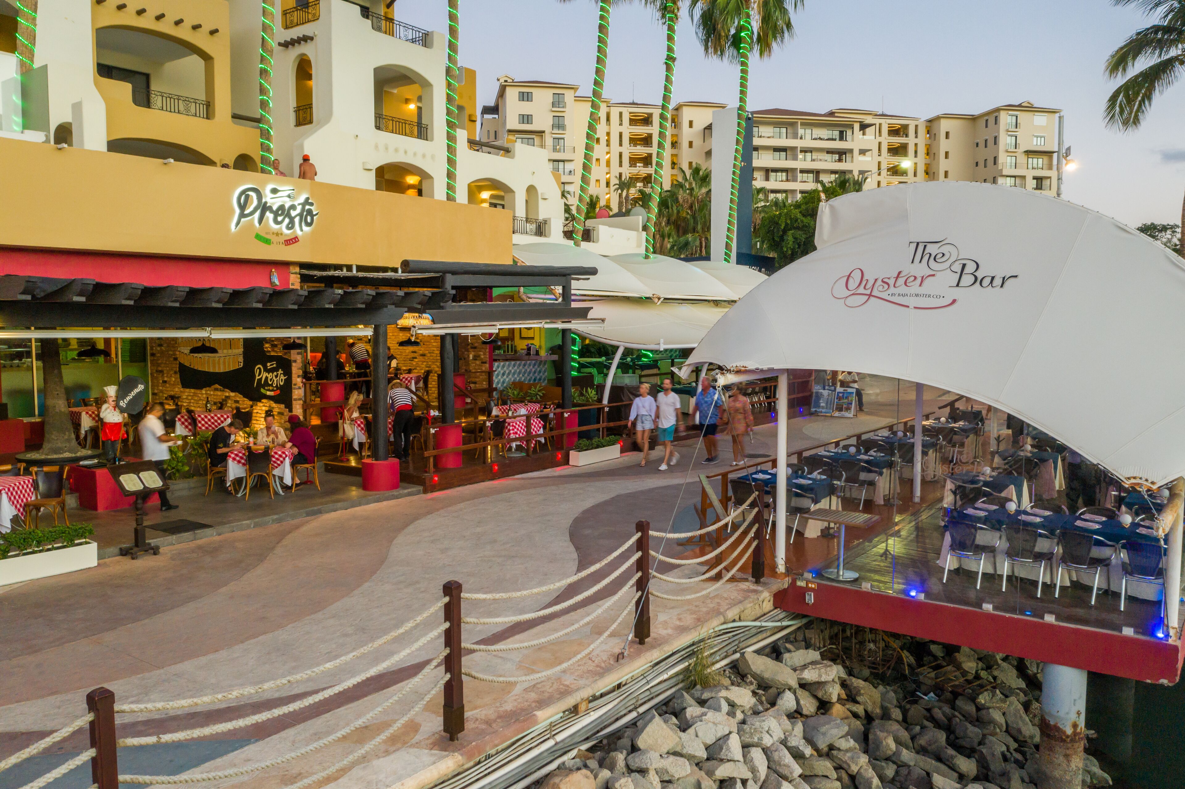 An outdoor dining area with tables and chairs, a restaurant named "Presto," and a bar named "The Oyster Bar."