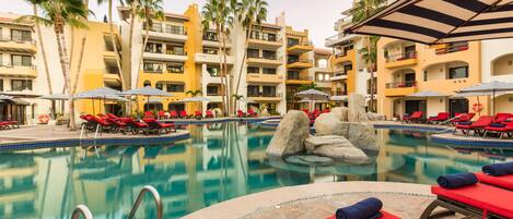 A hotel pool area with red lounge chairs, palm trees, and a clear blue pool.