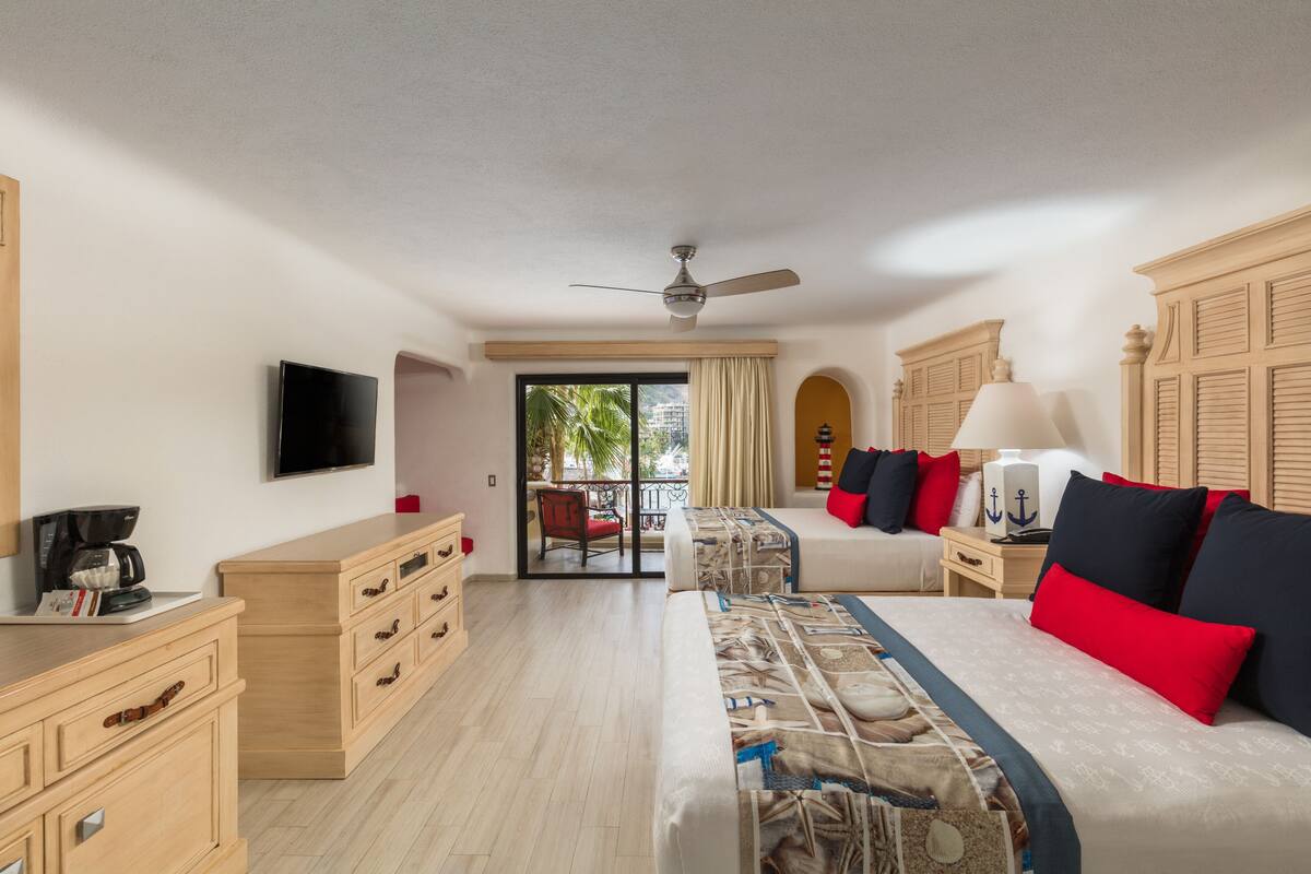 A hotel room with a bed, a desk, a chair, a television, and a window with a view of palm trees.