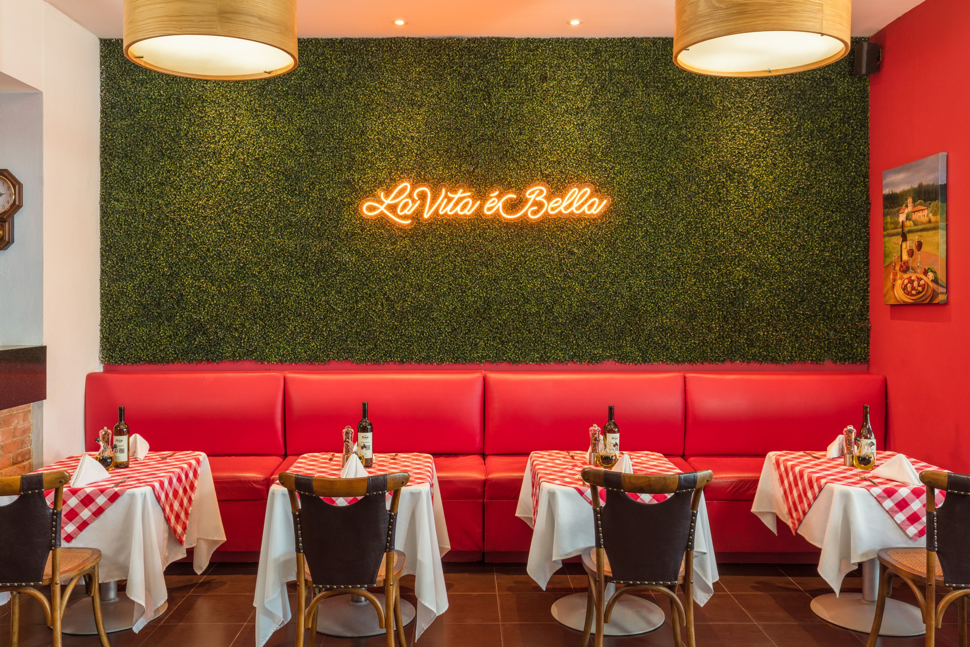 A restaurant interior with red seating, checkered tablecloths, and a neon sign reading "La Vita è Bella".