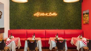 A restaurant interior with red seating, checkered tablecloths, and a neon sign reading "La Vita è Bella".