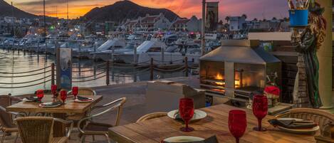 A waterfront restaurant with outdoor seating, a view of the marina, and a statue of a woman holding a bucket.