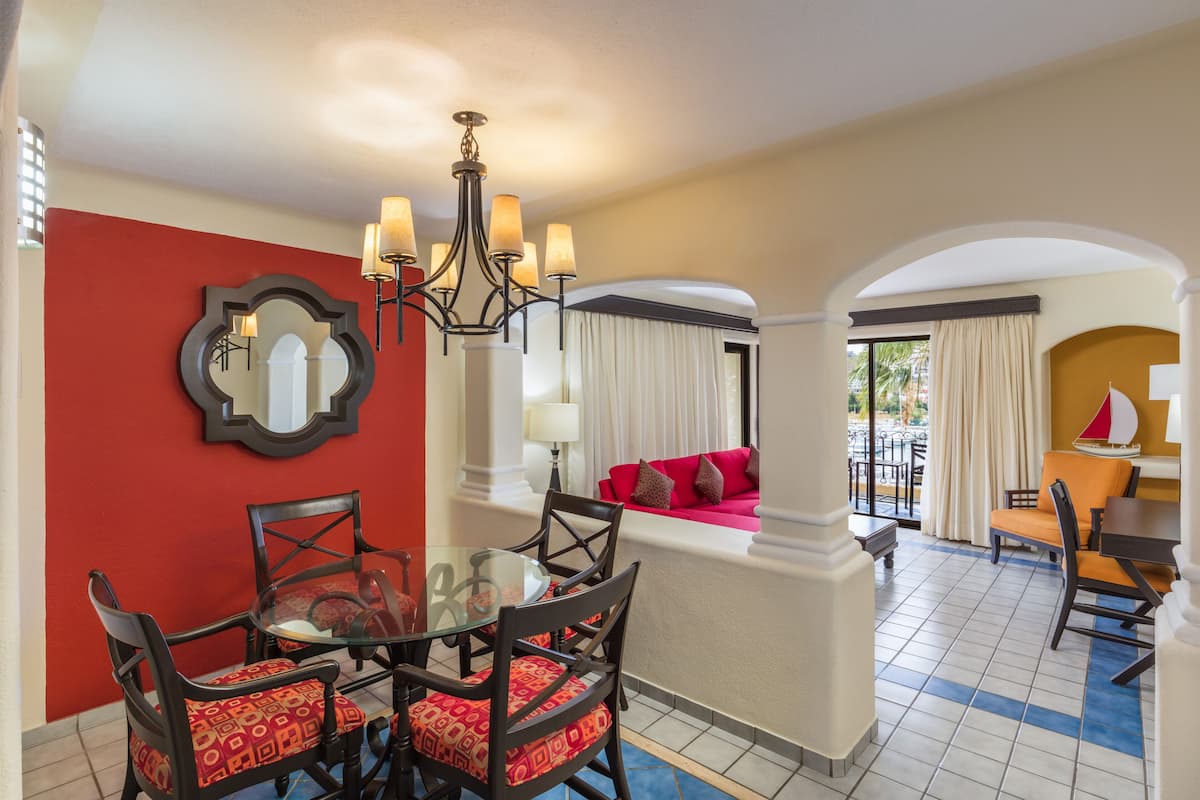 A dining area with a glass table and chairs, a chandelier, and a red accent wall.