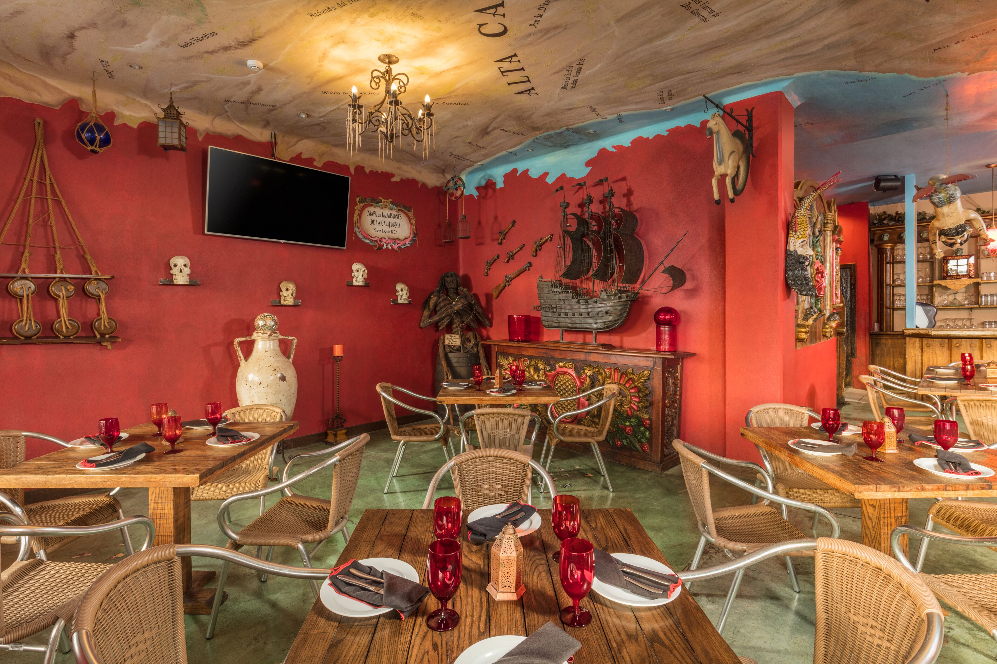A dining area with wooden tables and wicker chairs, decorated with red wine glasses and plates.