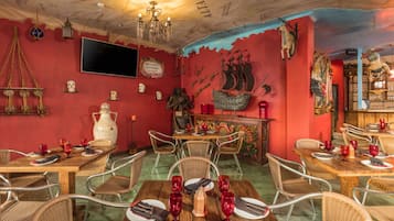 A dining area with wooden tables and wicker chairs, decorated with red wine glasses and plates.