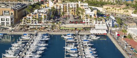 A marina with numerous boats docked, surrounded by a coastal town with buildings and a beach in the background.