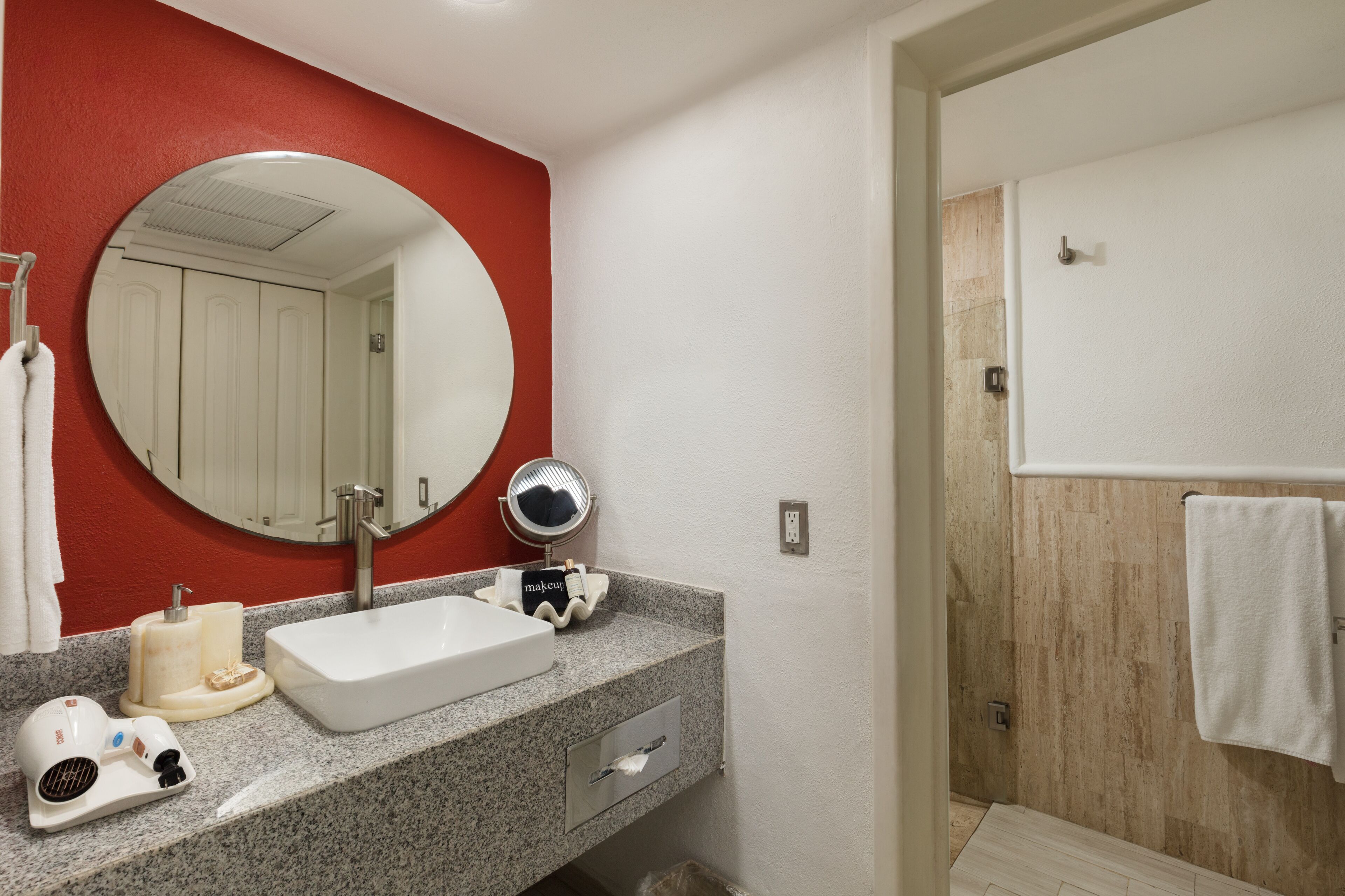 A bathroom with a white sink, a round mirror, a towel hanging on the wall, and a shower area.