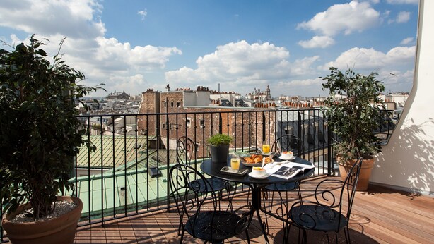 A balcony with a table set for breakfast, potted plants, and a view of the cityscape. - Hôtel Les 3 Poussins (Paris)