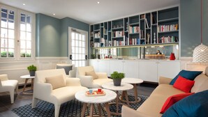 A modern living room with a sofa, armchairs, a coffee table, and a bookshelf. - Hôtel Les 3 Poussins (Paris)
