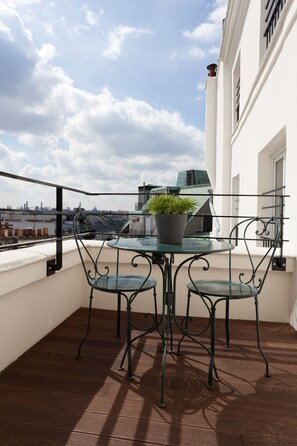 A balcony with a glass table and two chairs, a potted plant, and a city view. - Hôtel Les 3 Poussins (Paris)