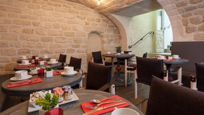 A restaurant with stone walls and tables set for dining. - Hôtel Les 3 Poussins (Paris)