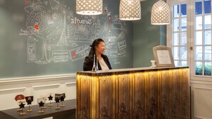 A reception desk with a chalkboard wall featuring doodles and text, two hanging pendant lights, and a window with a view. - Hôtel Les 3 Poussins (Paris)