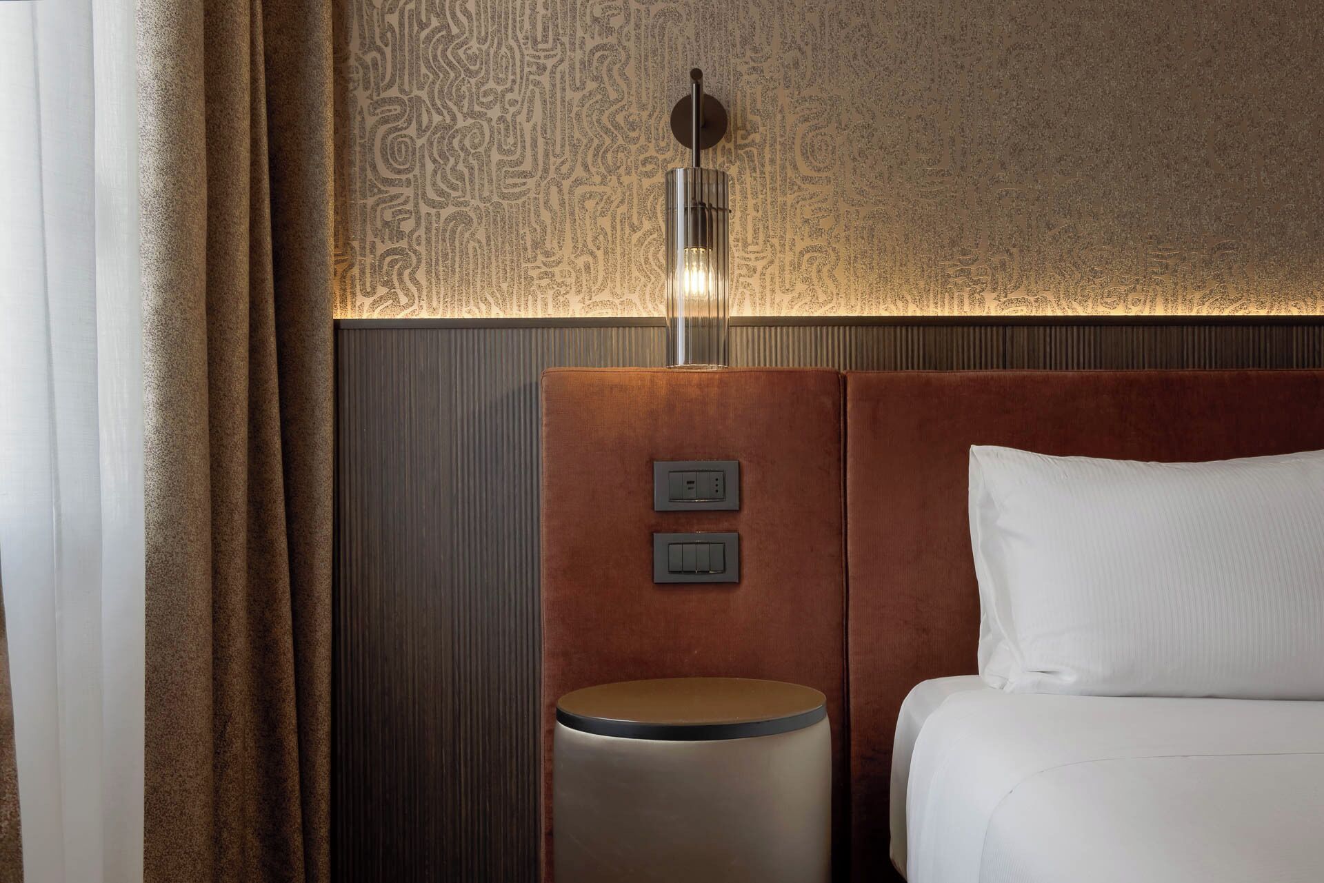 Ein Hotelzimmer mit einem Bett, einem Nachttisch mit Lampe und einer Wand mit Musterdesign.