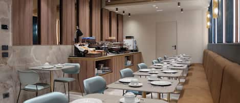 A modern dining area with a long counter, individual tables, and a seating area with a sofa.