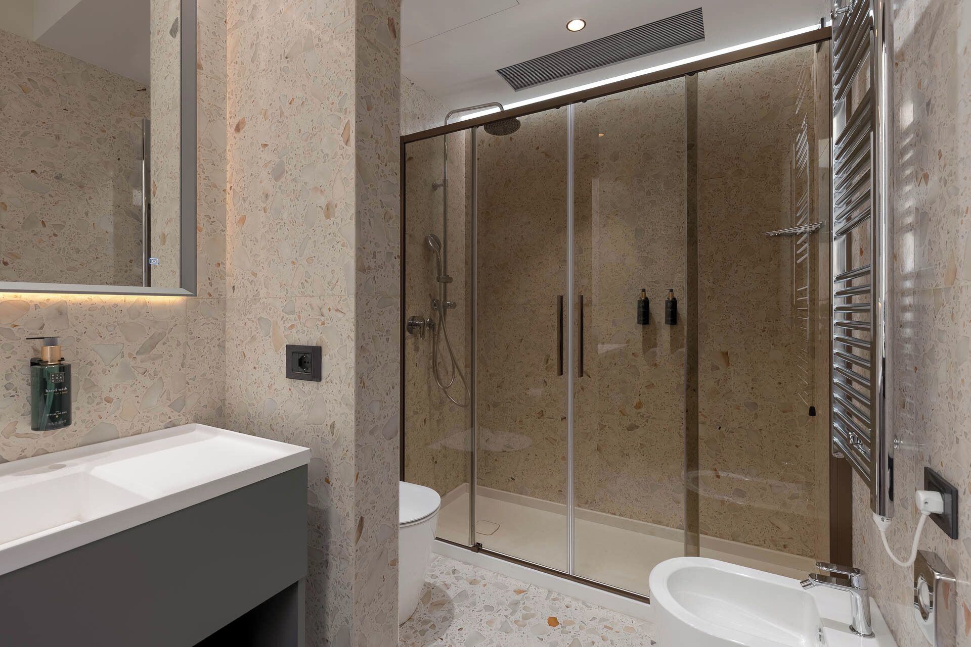 Un baño moderno con ducha envuelta en vidrio, lavamanos blanco y retrete.