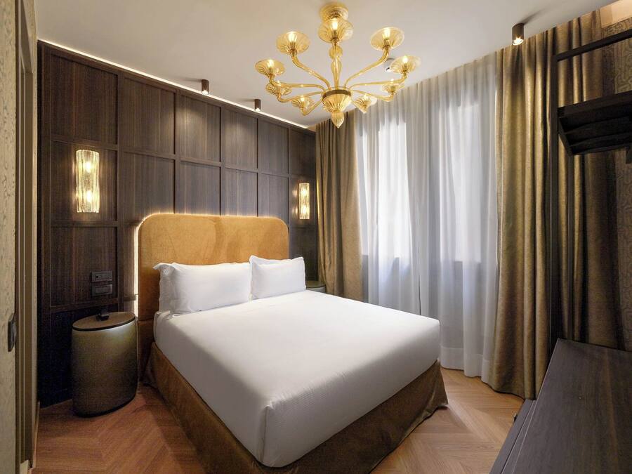 Una habitación de hotel con una cama grande, una araña, una mesita de noche y un televisor.