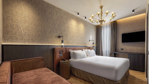 Quarto de hotel moderno com uma cama grande, área de estar, televisão e parede estampada.