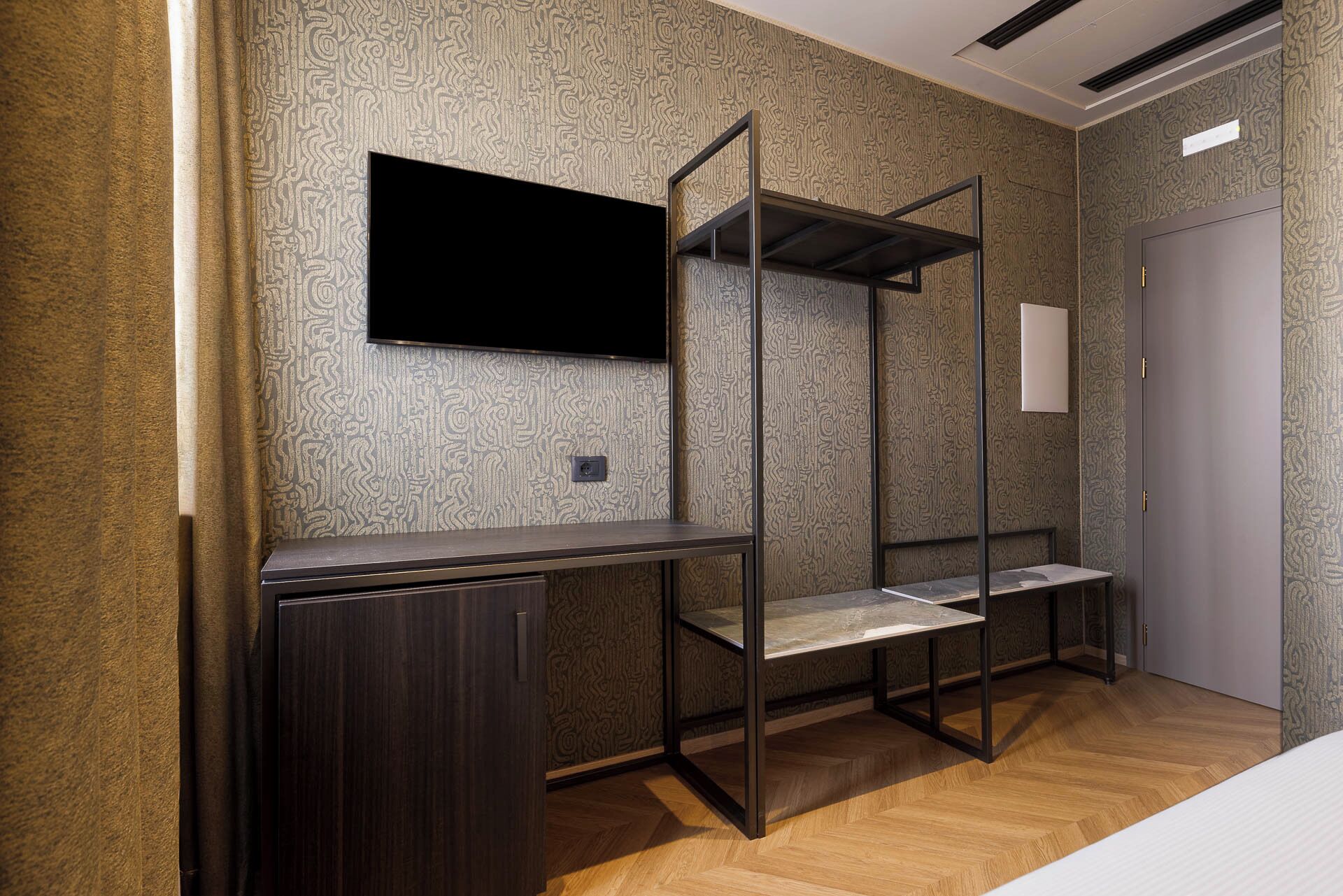 A room with a bunk bed, a flat-screen TV mounted on the wall, a desk, and a door.