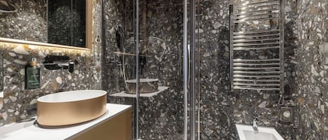 A modern bathroom with a marble backsplash, a round sink, a glass shower enclosure, and a bidet.