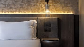 A hotel room with a bed, a bedside table, a wall-mounted light fixture, and a textured wall panel.