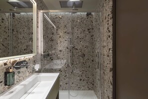Une salle de bain moderne avec un grand miroir, un lavabo blanc et une douche dotée d’une paroi en verre.