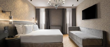 Un dormitorio moderno con una cama grande, un sofá, un televisor montado en la pared y un papel tapiz estampado.