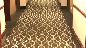 Ein Hotel-Flur mit gemustertem Teppich, Türen auf beiden Seiten und einem Licht am Ende.