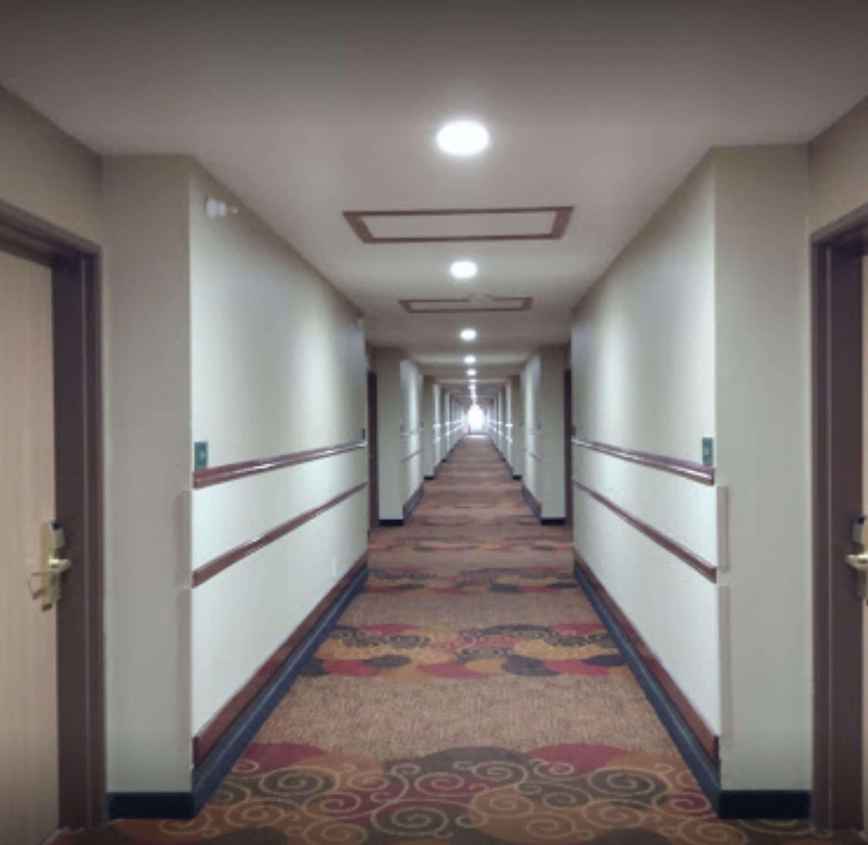 Een hotelgang met een vloerkleed, houten leuningen en deuren aan weerszijden.