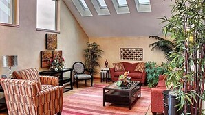 Ein Wohnzimmer mit schräg verlaufender Decke, einer Couch, einem Couchtisch und verschiedenen Pflanzen.