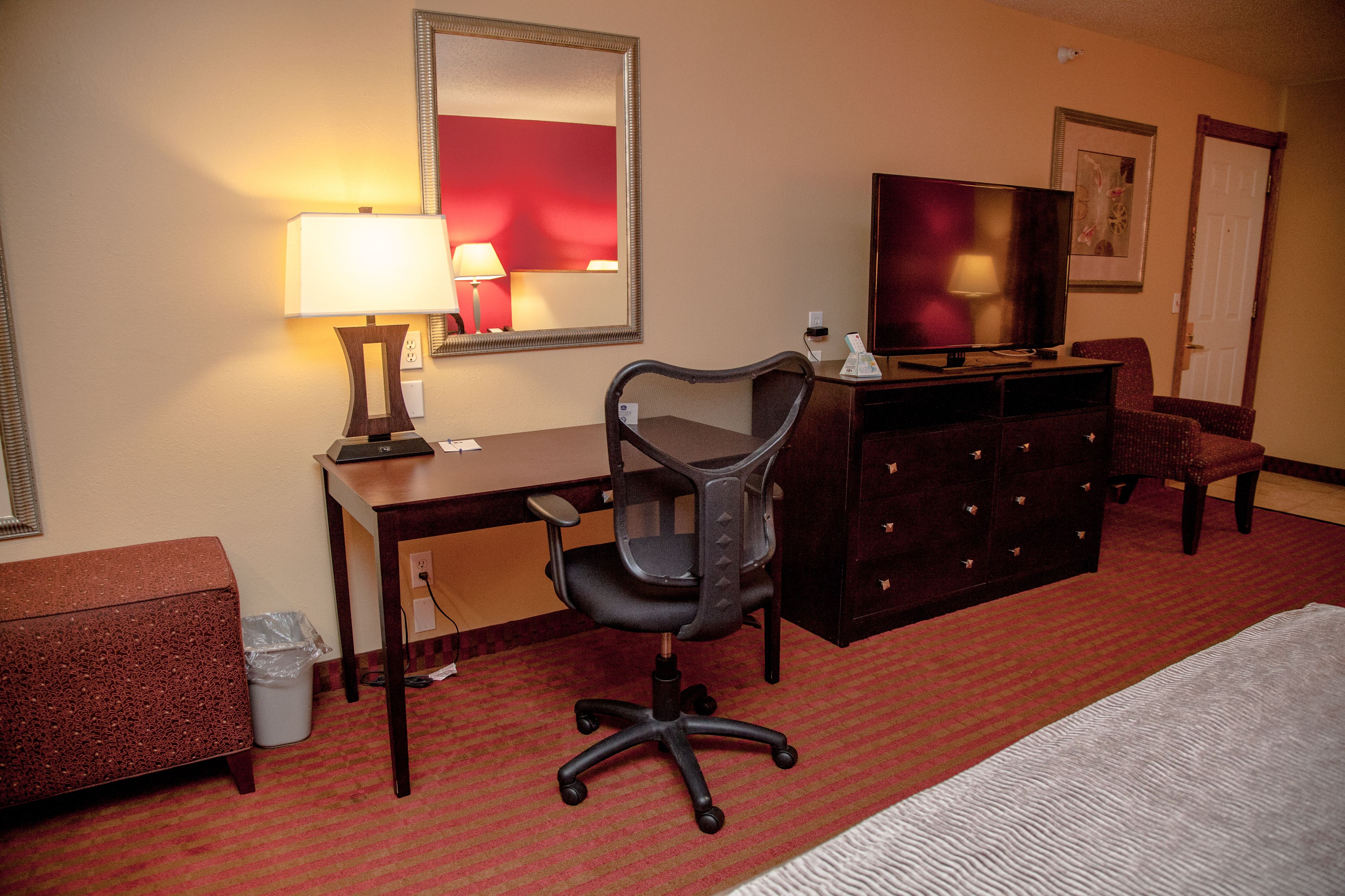 A hotel room with a desk, chair, TV, dresser, and a bed.