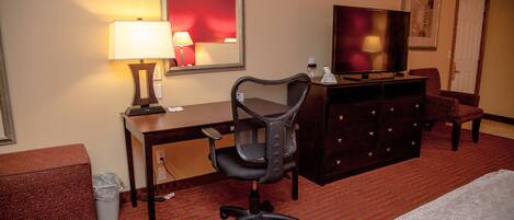 A hotel room with a desk, chair, TV, dresser, and a bed.