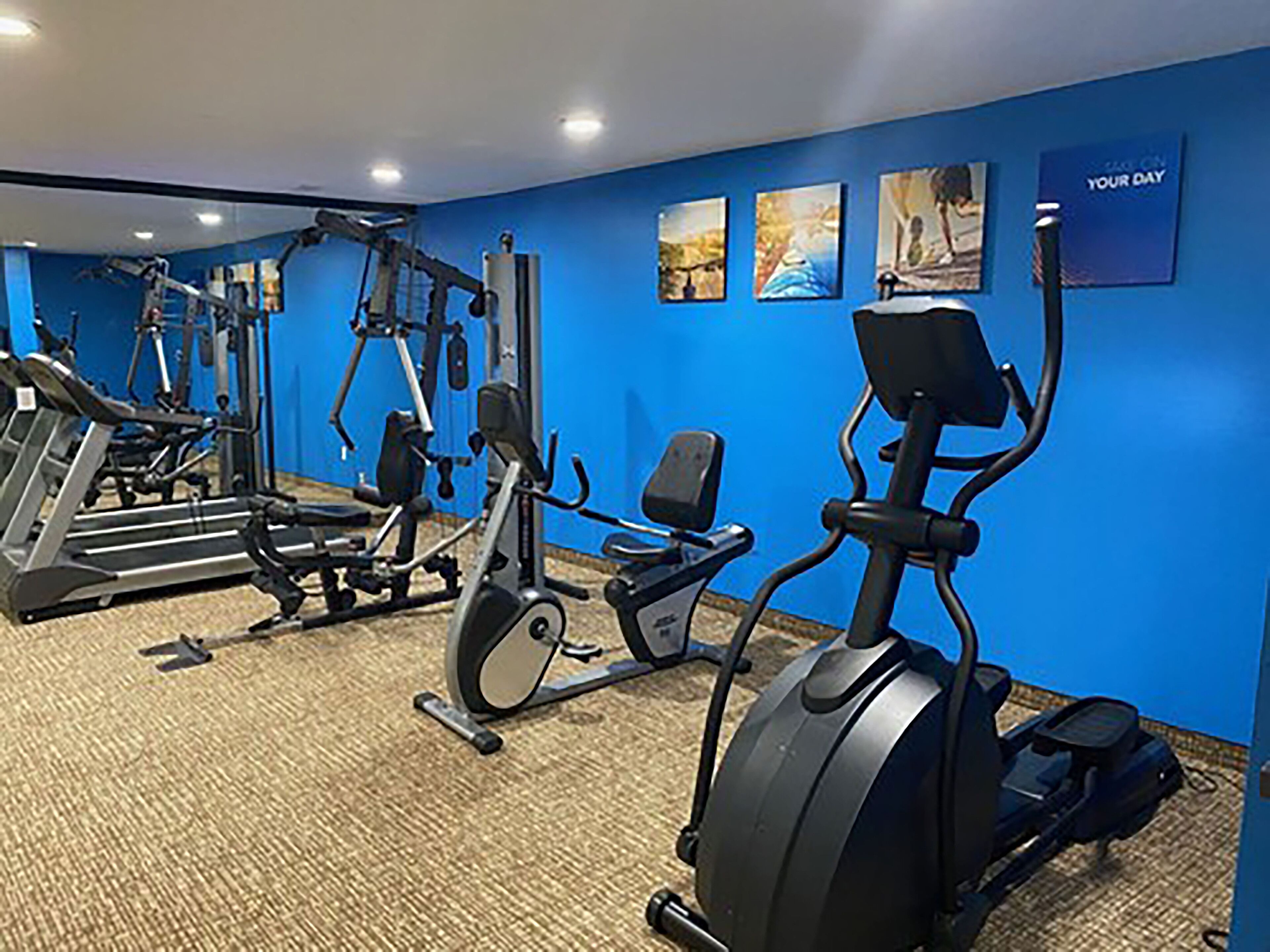 A gym with cardio machines, weight machines, and a wall with motivational artwork.