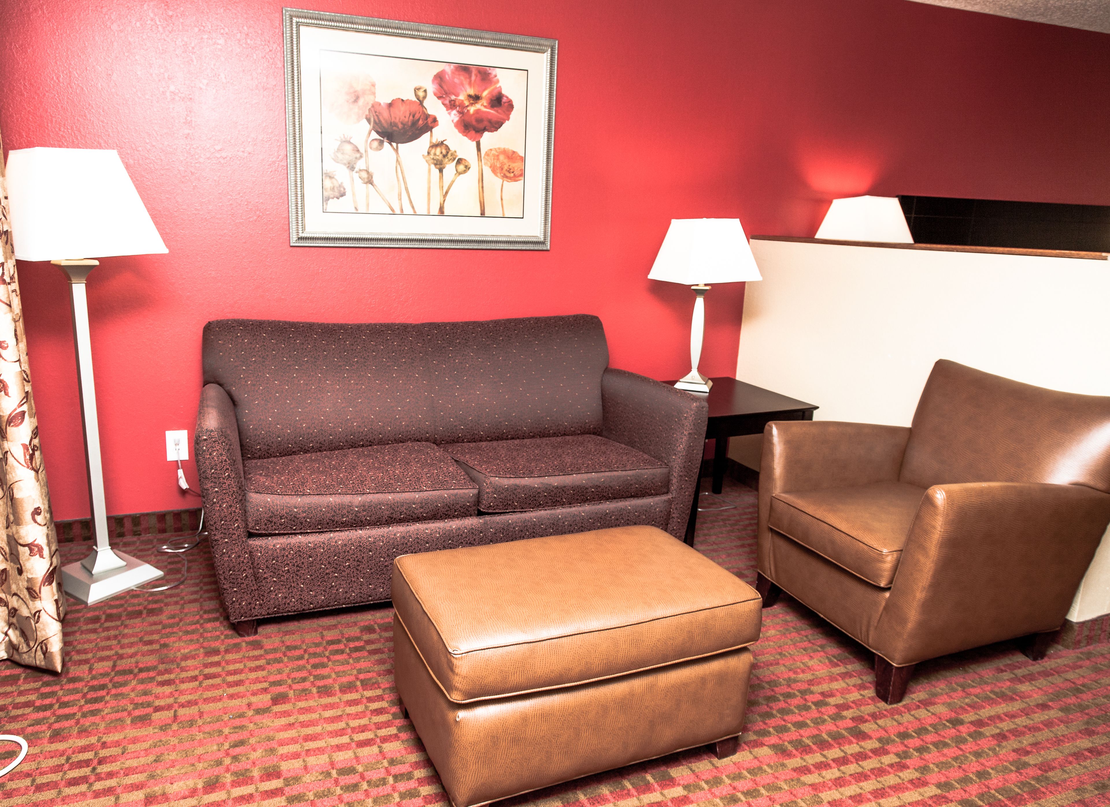 Una habitación con una pared roja, un sofá marrón, un sillón marrón, una mesita y una lámpara.