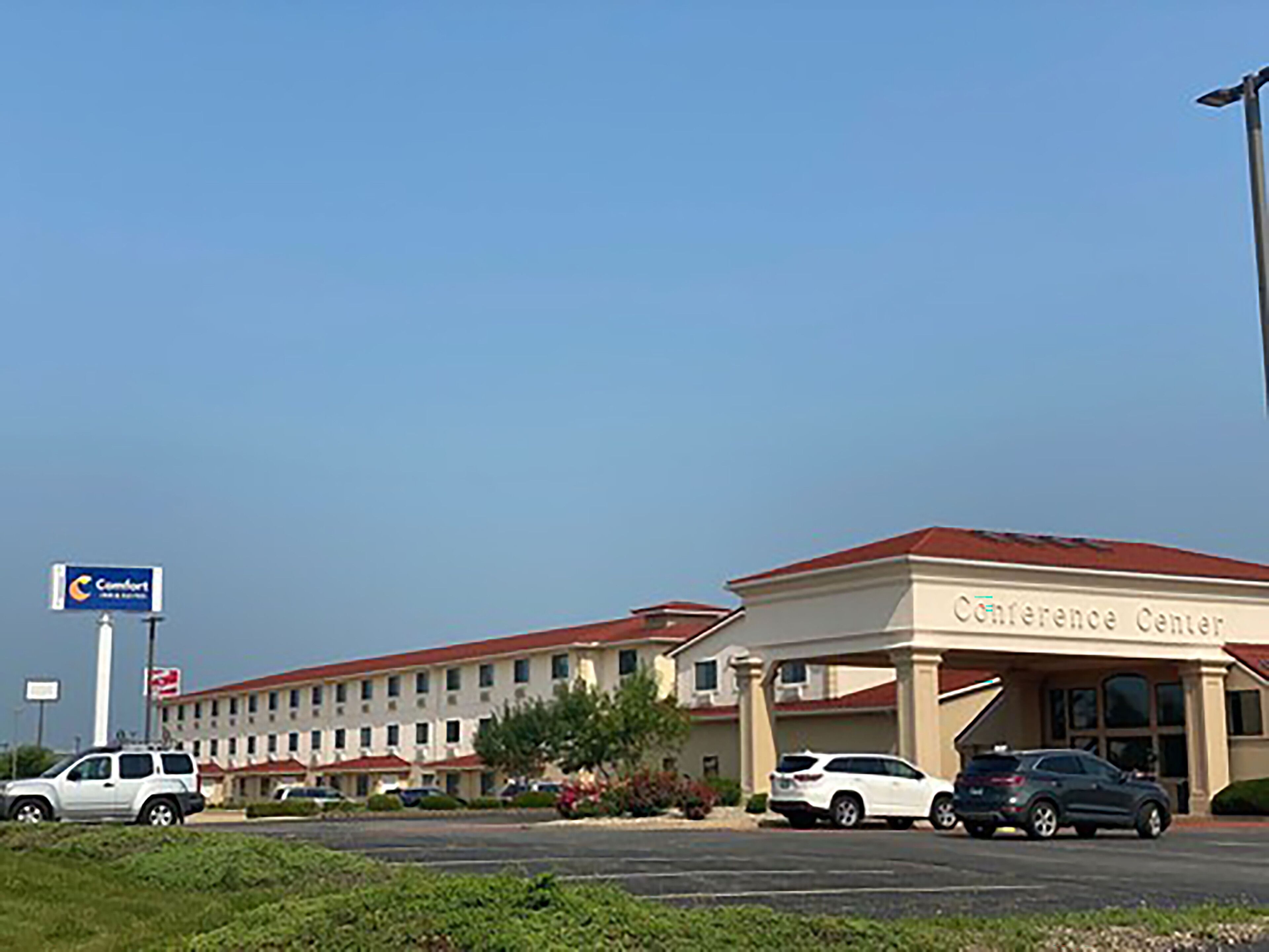 A hotel with a red roof and beige walls, named "Conference Center." There are several cars parked in front, and a sign for "Comfort" is visible.