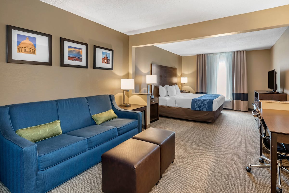 A hotel room with a blue sofa, a bed, a desk, and a TV.