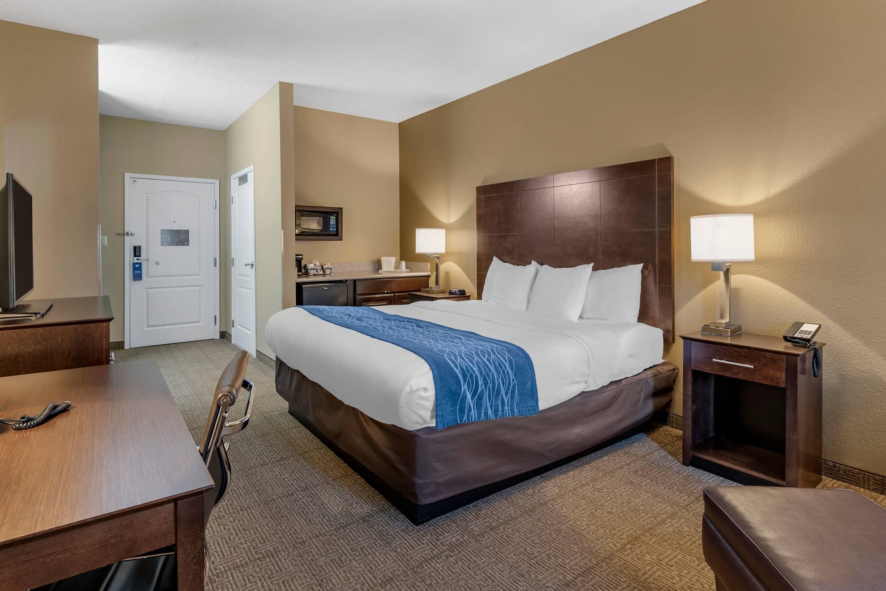 A hotel room with a large bed, a desk, a chair, a TV, a microwave, and a door.