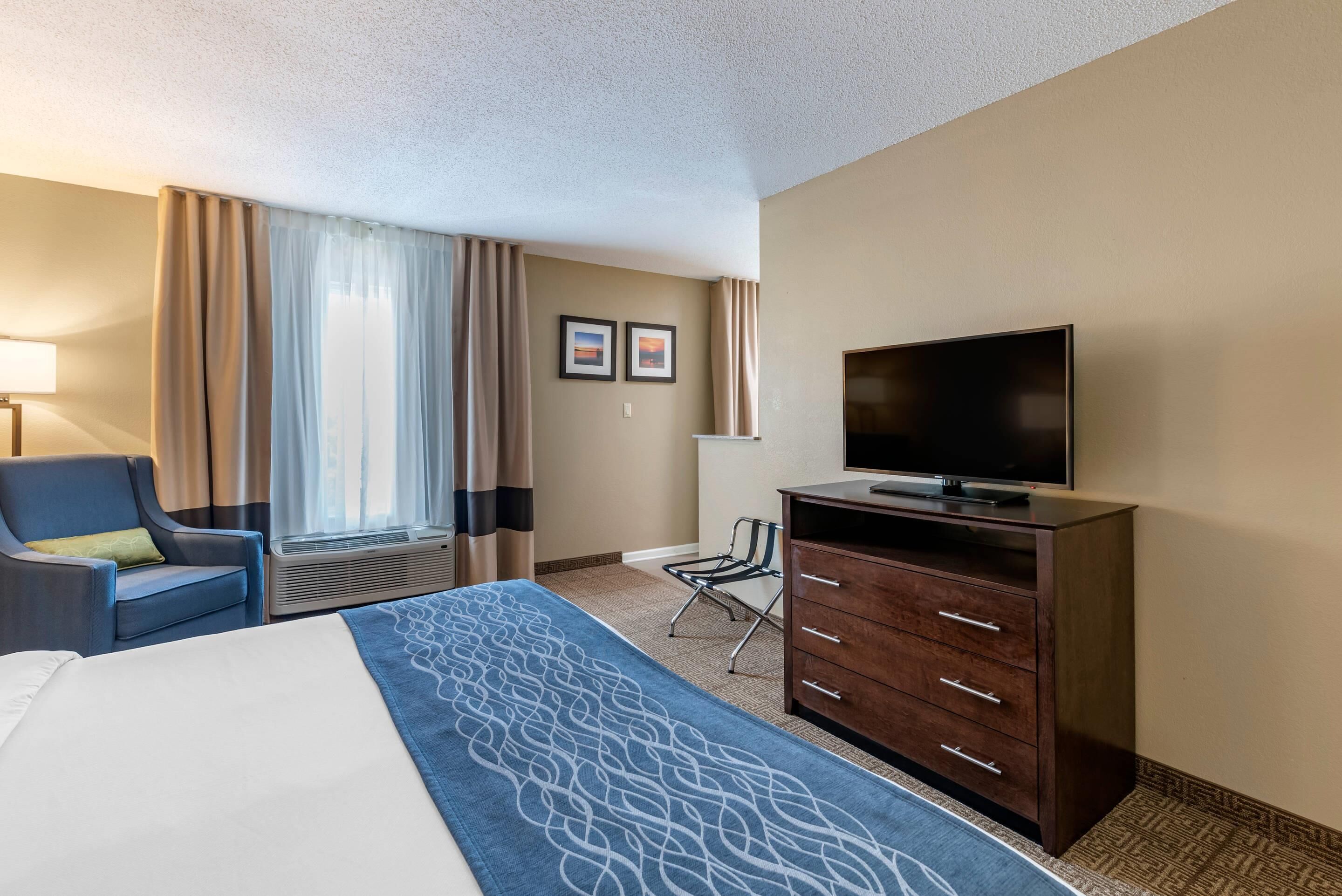 A hotel room with a bed, a TV, a desk, a chair, and a window with curtains.
