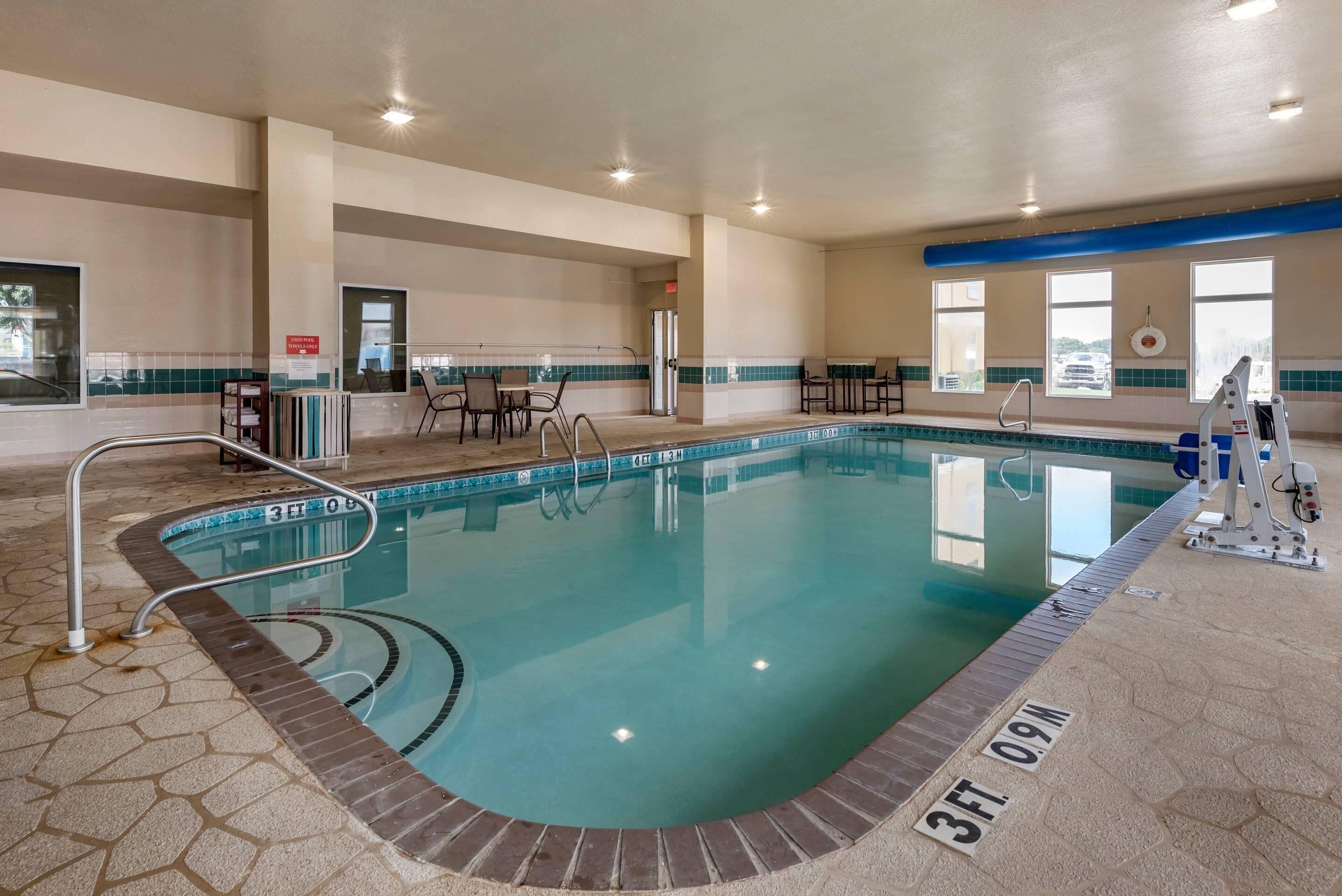 An indoor swimming pool with clear water, a lifeguard chair, and a changing room in the background.