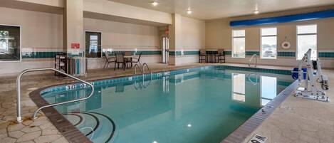 An indoor swimming pool with clear water, a lifeguard chair, and a changing room in the background.