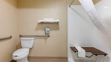 Une salle de bain équipée de toilettes, d’une douche avec un rideau blanc, d’une barre d’appui, d’une étagère avec des serviettes et d’un téléphone.