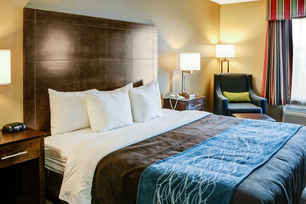 A hotel room with a large bed, bedside tables, a chair, a lamp, and a window with curtains.