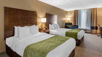 A hotel room with two beds, a desk, a chair, a lamp, and a large window with curtains.