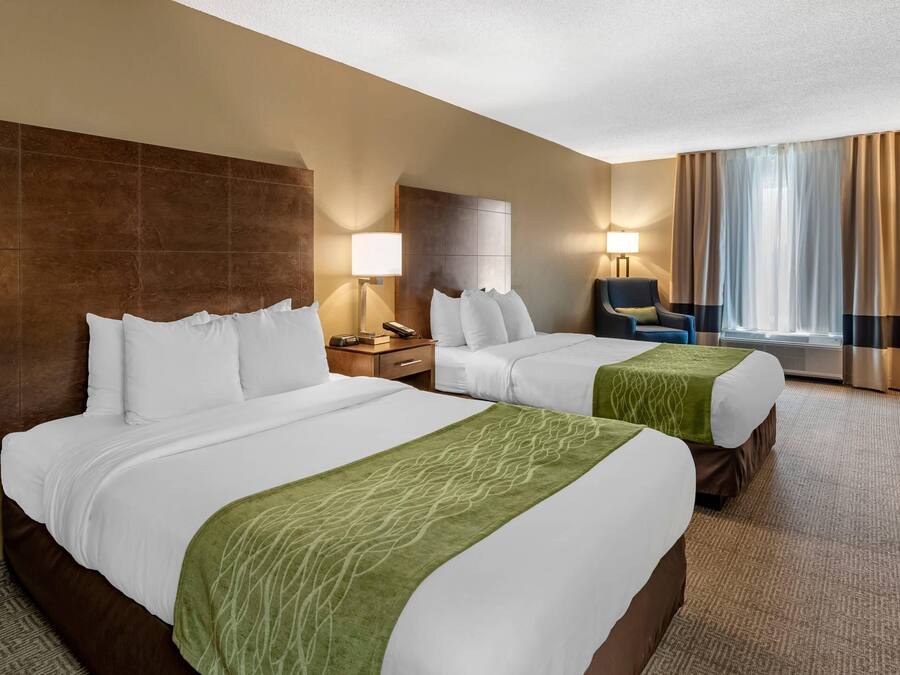 A hotel room with two beds, a desk, a chair, a lamp, and a large window with curtains.