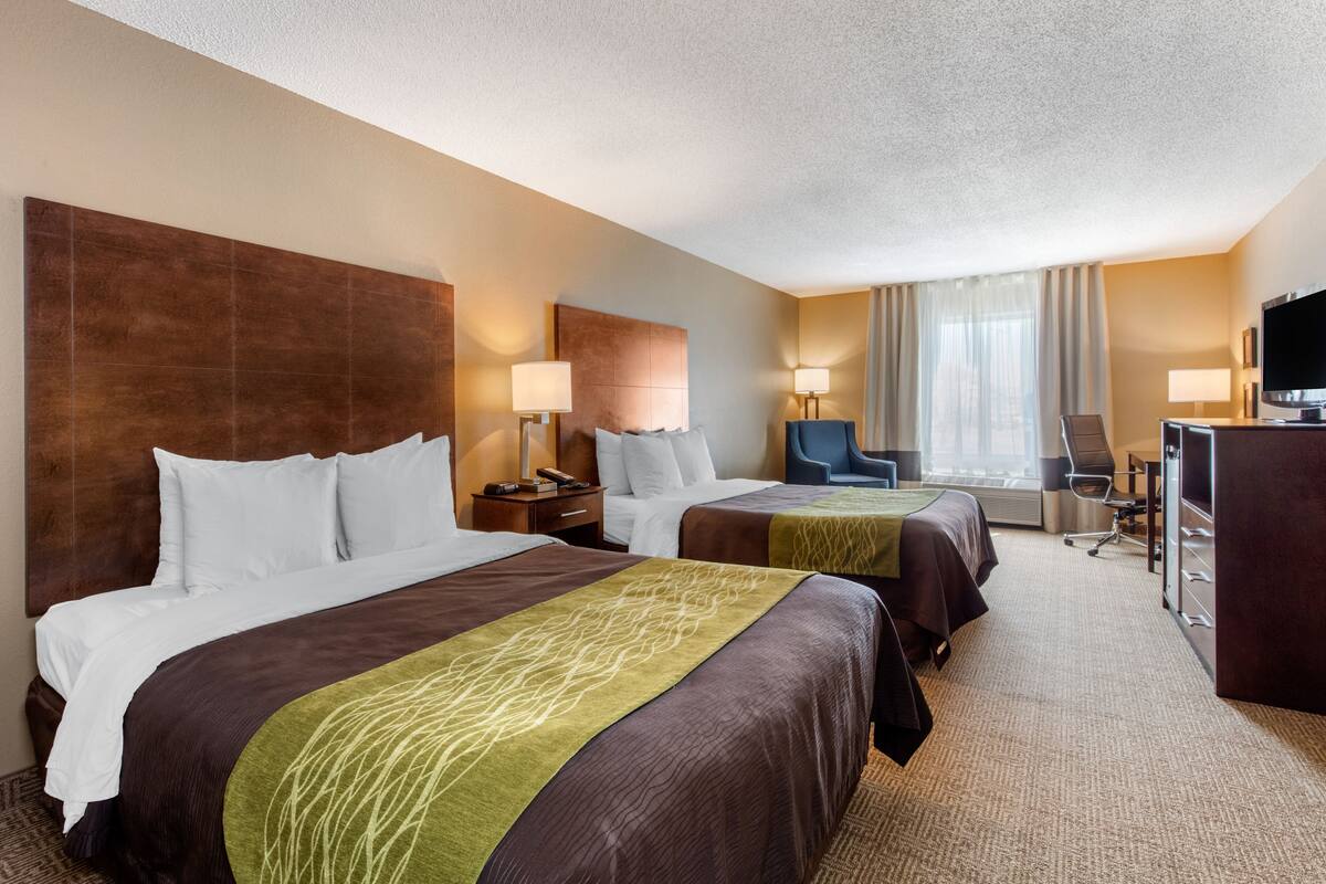 A hotel room with two beds, a desk, a chair, and a TV.