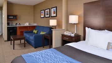 A hotel room with a bed, a sofa, a desk, a lamp, a telephone, and a microwave in the kitchen area.