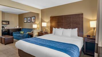A hotel room with a large bed, a desk with a chair, a sofa, and a small kitchenette.